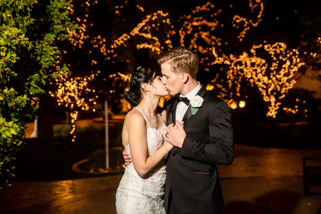 Bride and groom kissing under glowing string lights at a romantic nighttime Las Vegas wedding