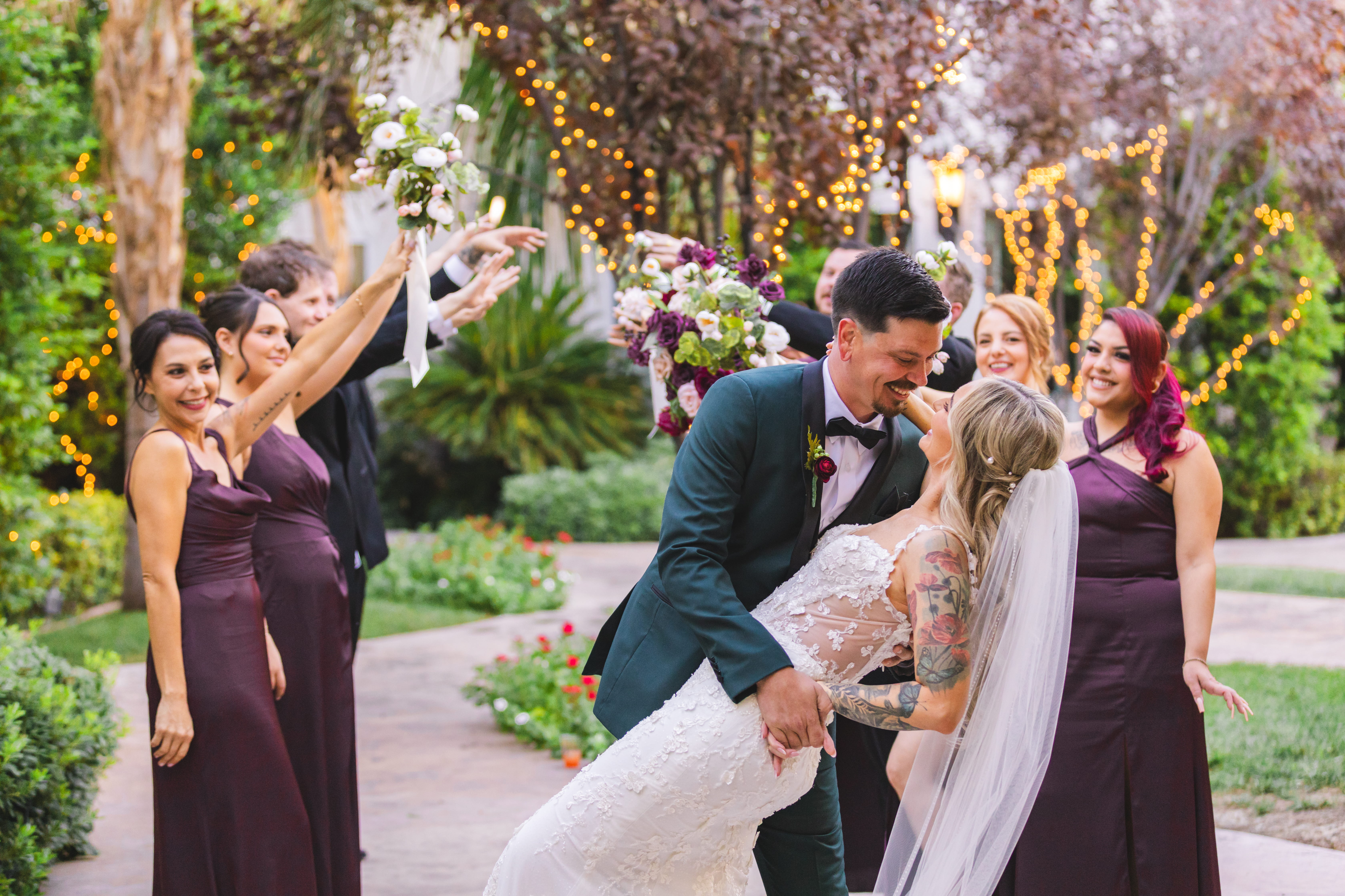 Groom dipping the bride for a kiss while bridesmaids celebrate around them in a garden wedding setting