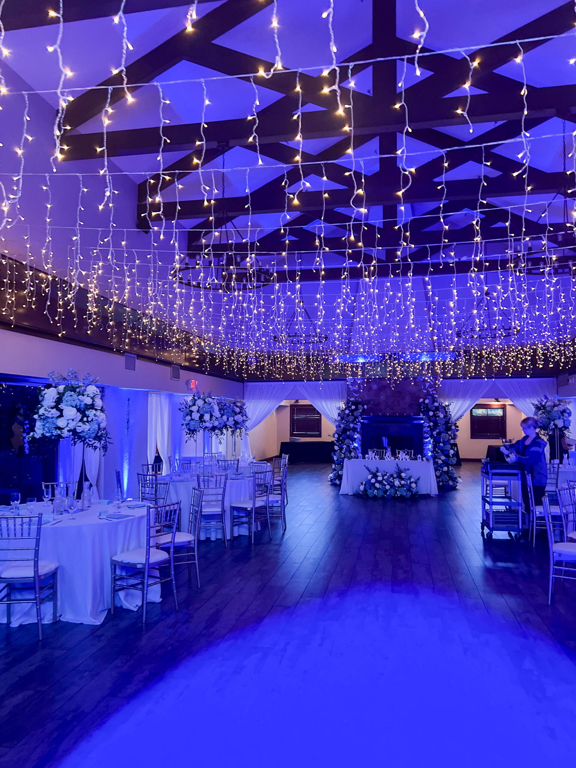 Las Vegas banquet hall reception with blue uplighting and ceiling draped in string lights over decorated tables