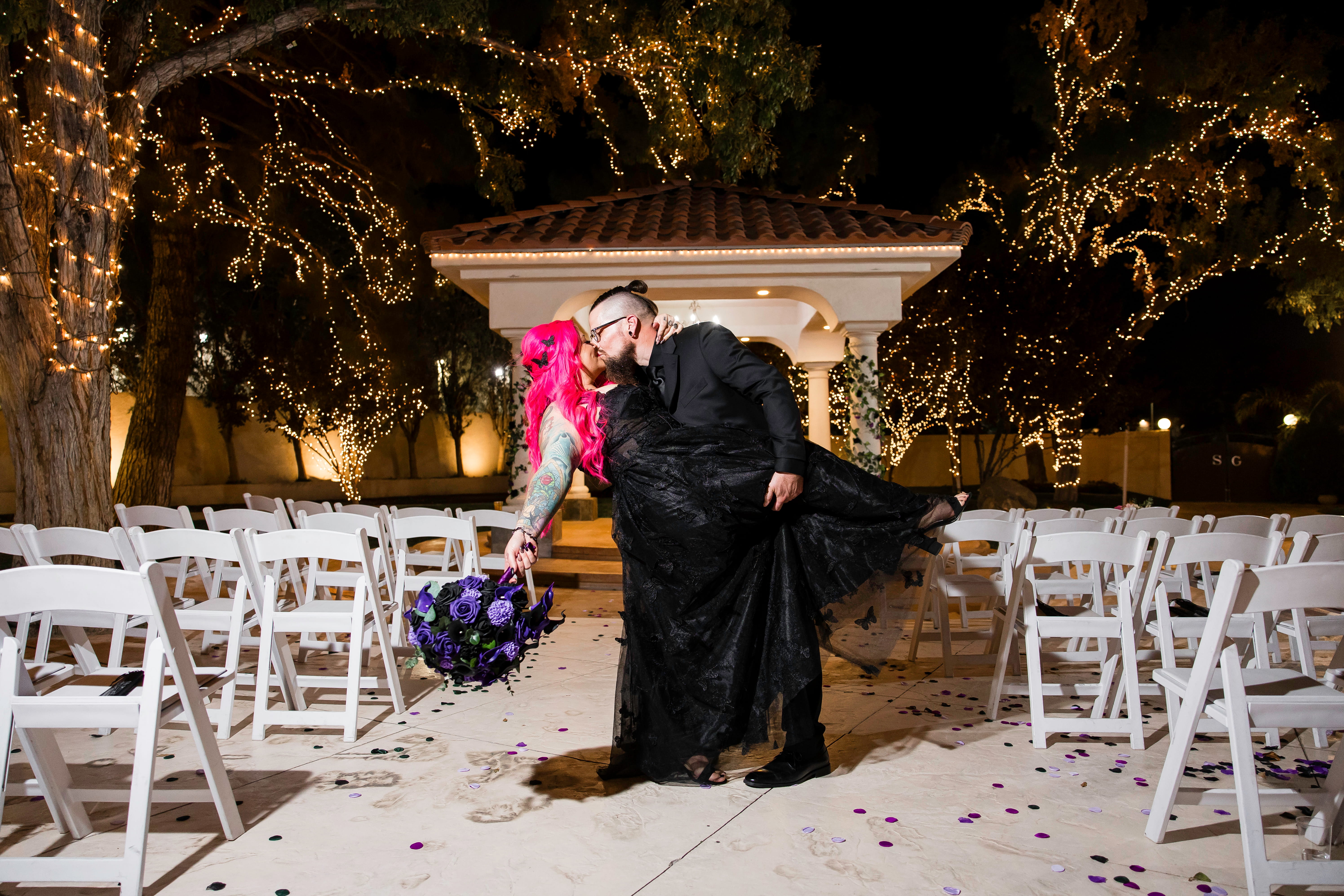 Couple sharing a kiss in front of a gazebo surrounded by twinkling lights during a nighttime wedding ceremony