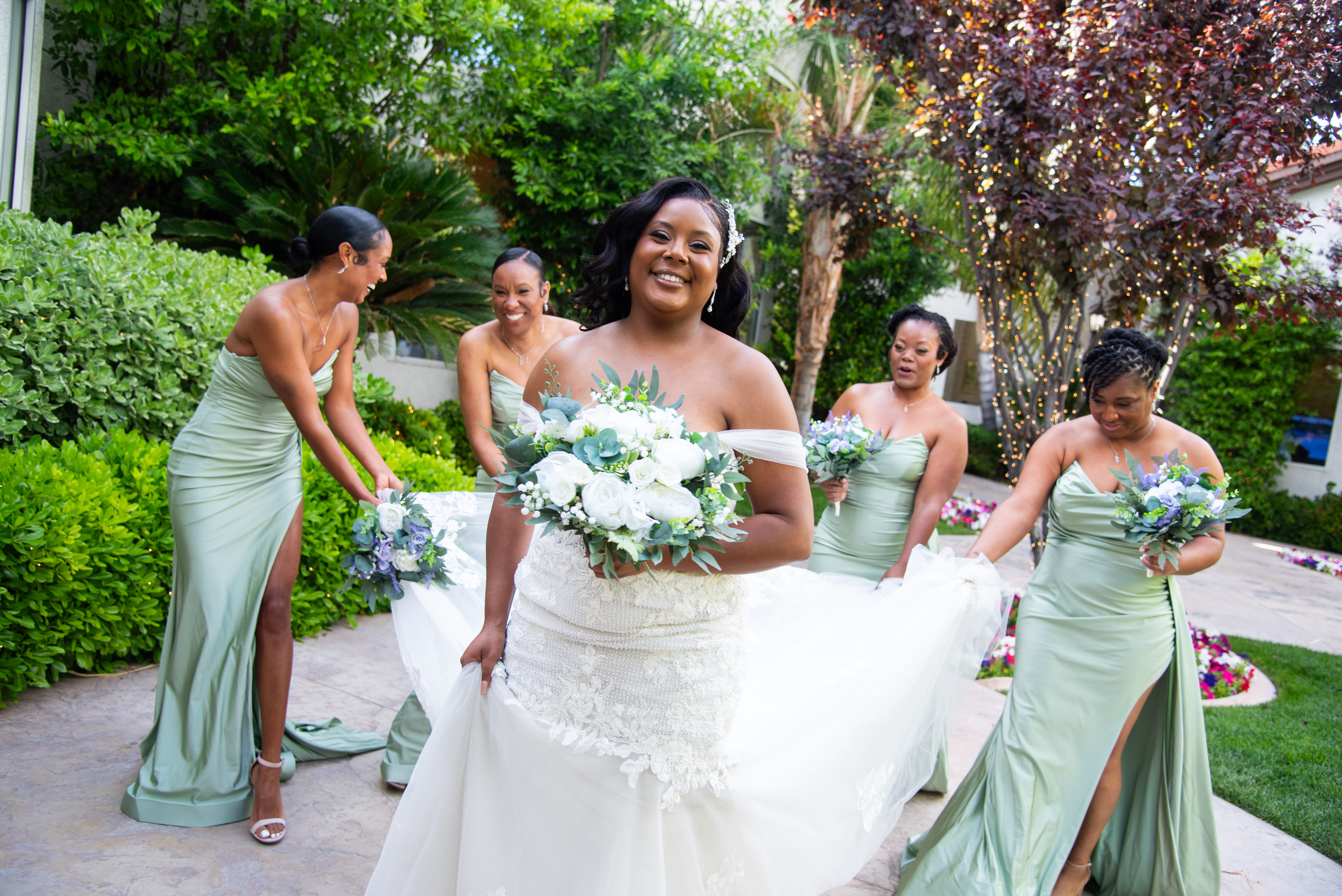 Bride laughing with bridesmaids in sage green dresses while getting ready at an outdoor Las Vegas wedding venue