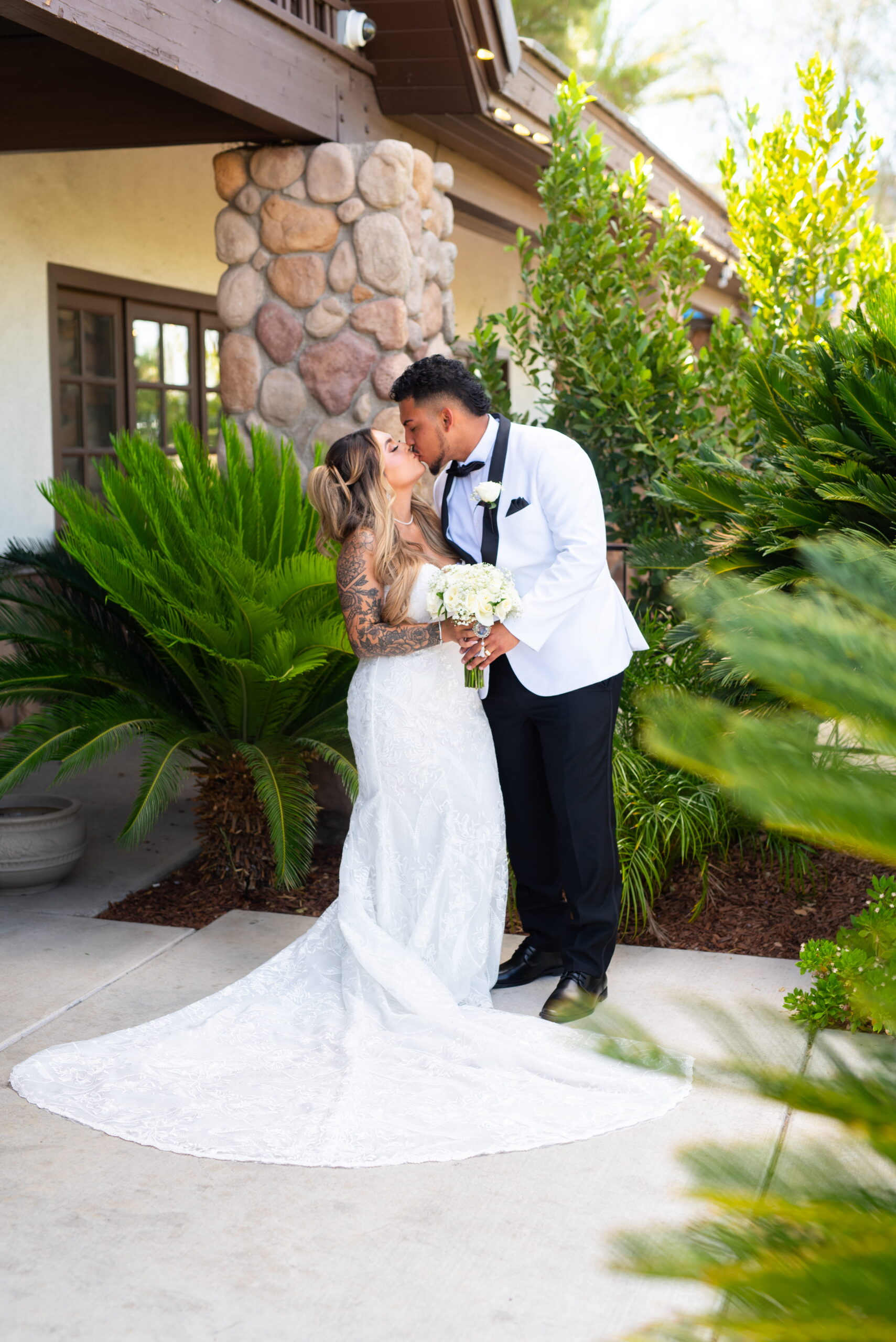 Bride and groom kissing in front of a stone-accented building surrounded by greenery at a Las Vegas wedding venue
