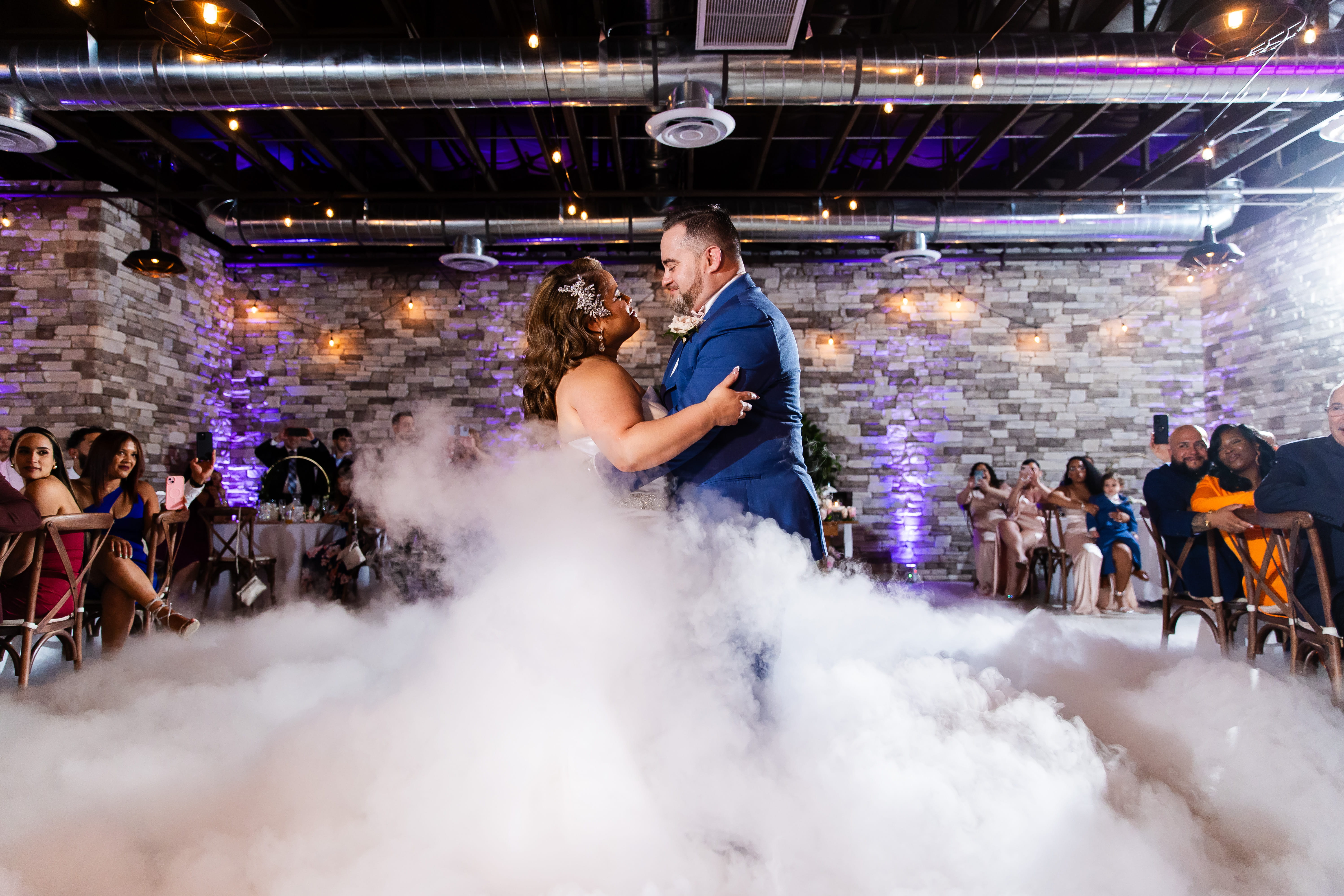 First dance inside indoor wedding venue Las Vegas with fog effect, uplighting, and stone wall backdrop 