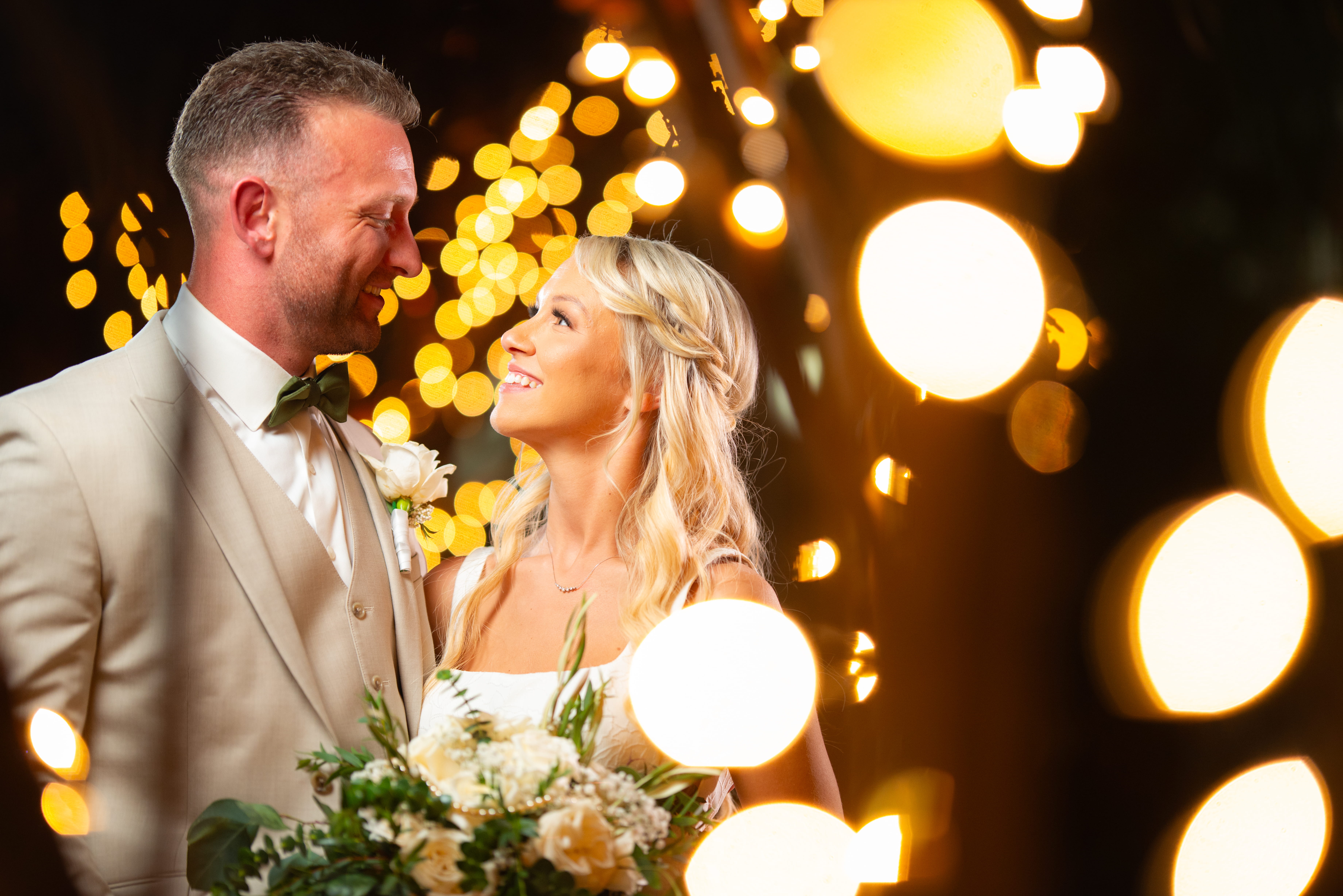 Newlywed couple smiling under warm string lights during an evening Las Vegas wedding at Sunset Gardens