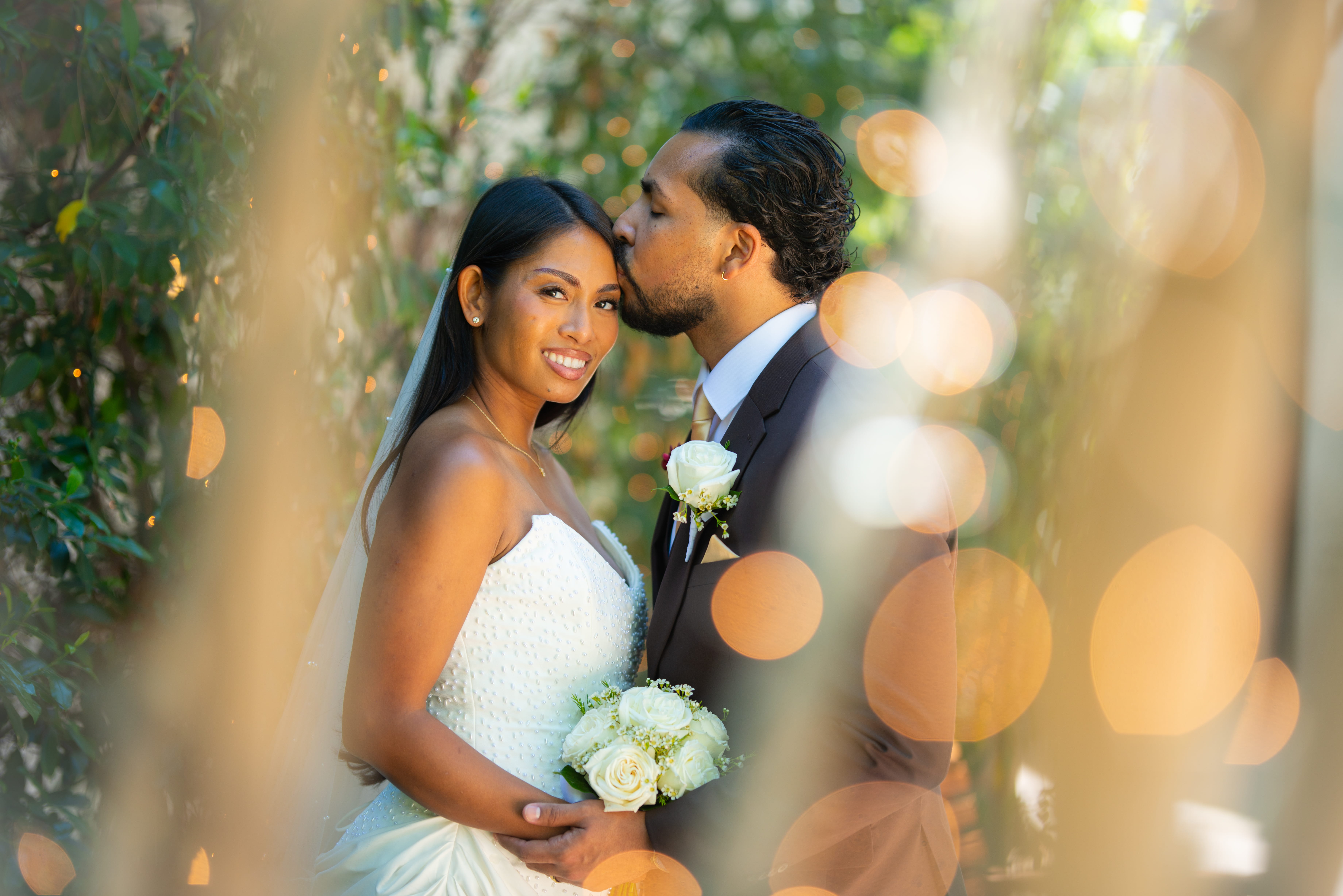 Bride and groom posing among greenery with soft glowing lights during a Las Vegas outdoor wedding photo session