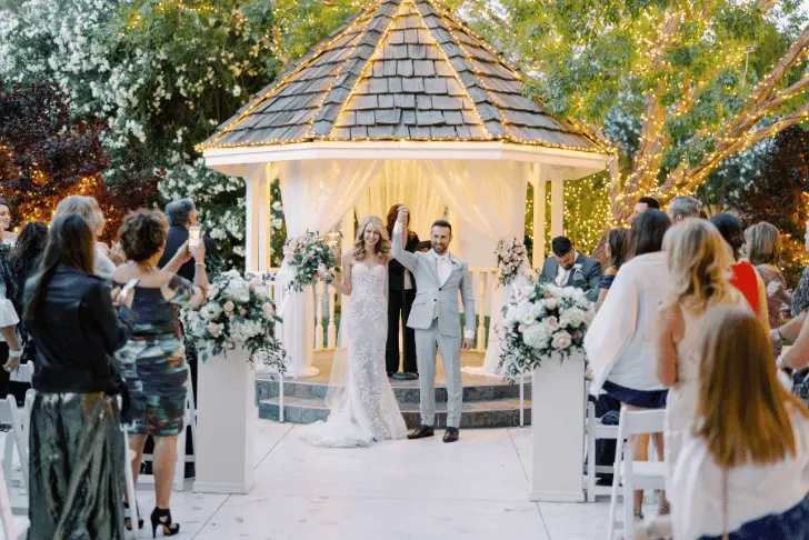 Wedding ceremony at Sunset Gardens gazebo with bride and groom celebrating surrounded by guests and floral arrangements